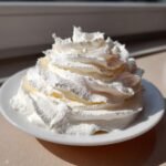 A generous swirl of bright white, fluffy Vanilla Frosting piled high on a small white saucer.