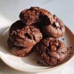 A stack of rich, dark brown Hot Chocolate Cookies piled on a light plate, featuring melted chocolate chips.