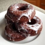 A stack of four rich, dark Glazed Chocolate Donuts topped with thick, white vanilla icing dripping down the sides.