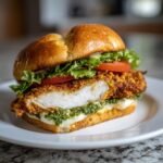 Close-up cross-section of a Green Goddess Crispy Chicken Sandwich showing crispy chicken, green goddess sauce, and fresh toppings.