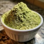 Close-up of a white bowl heaped high with vibrant green Homemade Ranch Seasoning Mix powder.