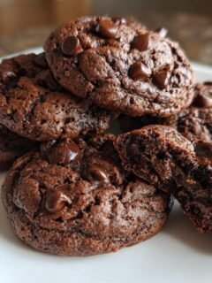 A stack of rich, dark Hot Chocolate Cookies on a white plate, one broken open showing a gooey center.