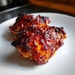 Two pieces of Irresistible Air Fryer BBQ Chicken Thighs with a thick, sticky, caramelized BBQ glaze on a white plate.