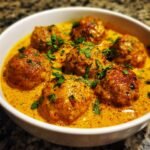 Close-up of several Irresistible Butter Chicken Meatballs simmering in a rich, creamy orange butter chicken sauce, garnished with cilantro.