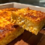 A close-up shot showing a square slice being lifted from an Irresistible Creamy Baked Corn Casserole, featuring a golden-brown crust and creamy corn filling.