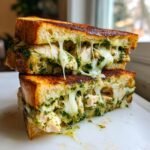Close-up of an Irresistible Mega Chicken Pesto Grilled Cheese Sandwich cut in half with melted cheese dripping.
