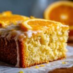 Close-up of a moist slice of Irresistible Orange Poppy Seed Cake topped with white glaze and fresh orange slices.