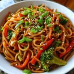 A close-up of Irresistible Sesame Peanut Veggie Noodles tossed in sauce, topped with sesame seeds and green onions.