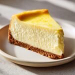 A perfect slice of creamy Lemon Cheesecake with a graham cracker crust, topped with bright yellow zest.