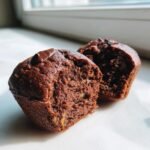 Close-up of a moist Chocolate Banana Muffins, cut open to show the texture and a melted chocolate chip on top.