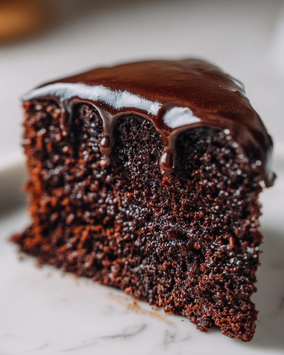 Close-up of a rich, dark slice of Chocolate Cake topped with dripping, glossy chocolate ganache.