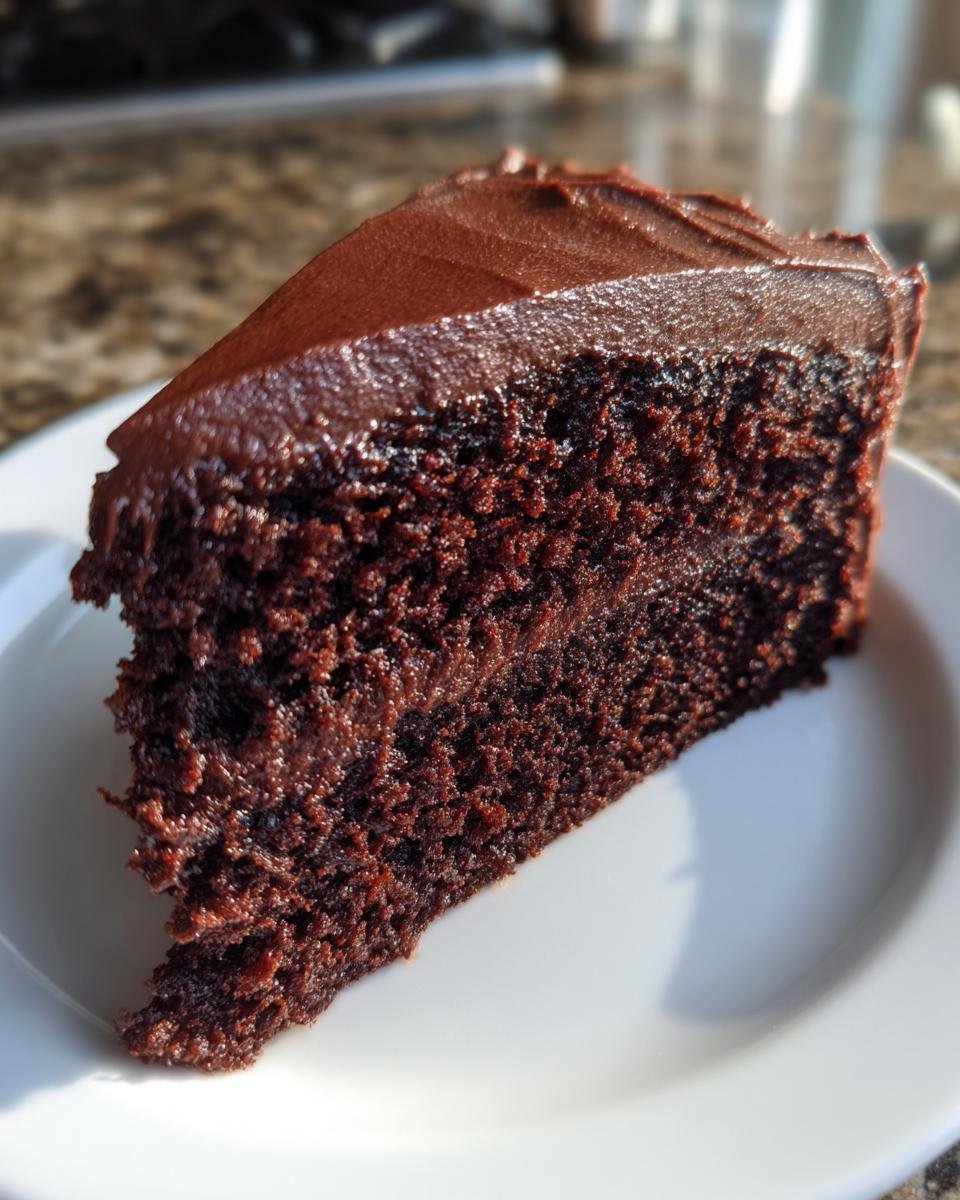 Close-up of a rich, dark slice of Chocolate Cupcake Cake topped with thick, glossy chocolate frosting.