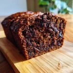 A close-up, cross-section view of a moist Chocolate Zucchini Bread loaf sitting on a wooden cutting board.