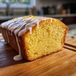 A close-up of a freshly baked Lemon Loaf Cake with thick white glaze dripping down the side.