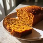 A close-up of a freshly baked loaf of moist Pumpkin Bread with one slice cut and resting beside it.