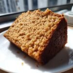 A close-up of a moist, golden-brown slice of Brown Sugar Cake resting on a white plate.