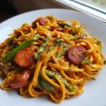 A close-up of One Pot Creamy Cajun Pasta Delight featuring linguine coated in orange sauce, sliced smoked sausage, and green bell peppers.