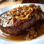 A juicy steak generously covered in rich, brown Onion Gravy Smothered Steak with caramelized onions.