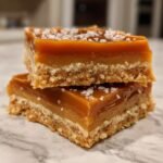 Two stacked Peanut Butter Caramel Bars with a thick, glossy caramel layer topped with flaky sea salt.