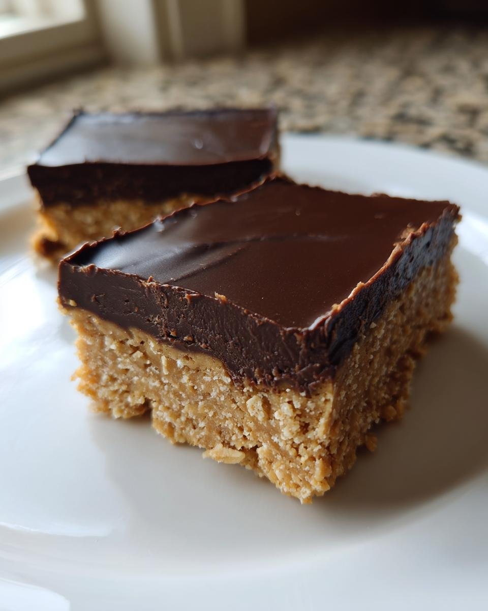 Two squares of rich Peanut Butter Chocolate Bars with a thick chocolate topping on a white plate.