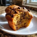A close-up view of a Peanut Butter Chocolate Chip Muffin, with a bite taken out, revealing a moist interior packed with chocolate chips.