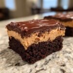 A decadent square slice of Peanut Butter Frosted Brownies showing a dark chocolate base, thick peanut butter layer, and chocolate ganache topping.
