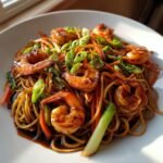 A close-up of delicious Shrimp Lo Mein noodles tossed in dark sauce, topped with glazed shrimp and fresh green onions.