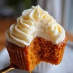 Close-up of a Pumpkin Cupcake Cake with a bite taken out, revealing the moist orange crumb and thick cream cheese frosting.