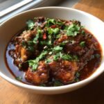 Close-up of rich, dark red Chicken Rogan Josh garnished generously with fresh cilantro.