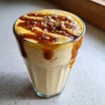 Close-up of a thick Salted Caramel Banana Milkshake topped with caramel drizzle and sea salt flakes.