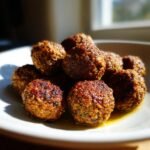 A close-up, sunlit shot of several golden-brown, seared Veggie Meatballs piled on a white plate.