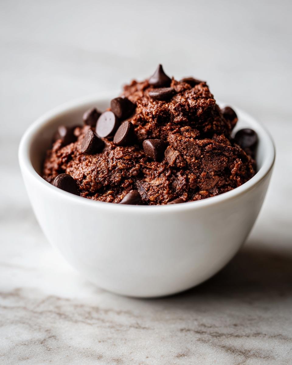 A small white bowl filled with rich, dark Chocolate Granola topped with chocolate chips.
