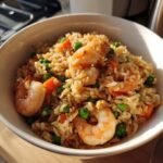 Close-up of a white bowl filled with savory Shrimp Fried Rice, featuring plump shrimp, peas, and carrots.