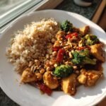 A plate of Skinny Cashew Chicken stir-fry with broccoli, peanuts, and a side of brown rice.