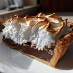 A close-up slice of Chocolate Meringue Pie showing a dark chocolate filling and fluffy, toasted meringue.