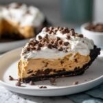 A decadent slice of Peanut Butter Pie with a dark crust, creamy filling, whipped cream, and mini chocolate chips.
