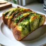 Four slices of golden-crusted Slow Cooker Basil Pesto Bread showing vibrant green pesto swirls on a white plate.