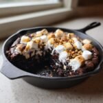 A gooey Smores Brownie Skillet topped with toasted marshmallows and graham cracker crumbs.