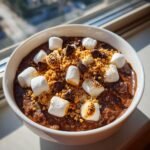 A close-up of Smores Overnight Oats topped with toasted marshmallows, chocolate chips, and graham cracker crumbs.