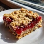 A single square of a Strawberry Oat Bars showing a thick layer of bright red jam filling between the oat crust and crumble topping.