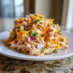 A close-up, mounded serving of Tex Mex Chicken Salad mixed with shredded cheese, red onion, and cilantro on a white plate.