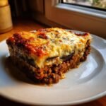 A thick, layered slice of Ultimate Greek Moussaka with rich meat filling and golden b&eacute;chamel topping.