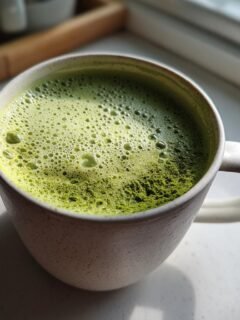 A close-up of foamy, bright green 4 Ingredient Matcha Hot Chocolate in a speckled white mug.