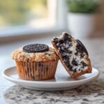 Two Bakery Style Oreo Muffins At Home, one whole with a cookie on top, and one cut in half showing the chocolate cookie chunks inside.