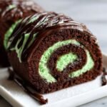 A cross-section of an Irresistible Chocolate Peppermint Swiss Roll showing dark chocolate cake and bright green mint filling.