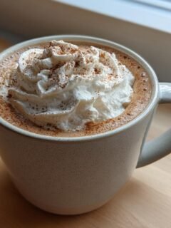 A close-up of a Cozy Gingerbread Latte Recipe topped with whipped cream and a dusting of cinnamon.