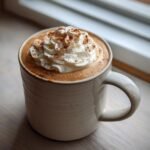 A cozy gingerbread latte topped with whipped cream and a dusting of cinnamon in a speckled mug.