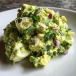 A mound of Creamy Avocado Egg Salad No Mayo Flavorful Healthy mixed with chunks of hard-boiled egg and red onion.