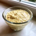 Close-up of thick, creamy Caesar salad dressing recipe in a small glass bowl, showing flecks of pepper and seasoning.