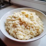 Close-up of a white bowl filled with rich, creamy simple risotto, showing the texture of the rice.